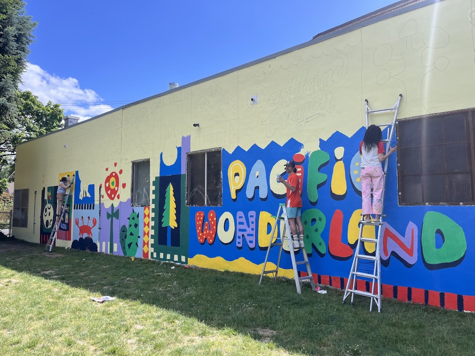 Volunteers on ladders painting the 'Pacific Wonderland' section of the mural