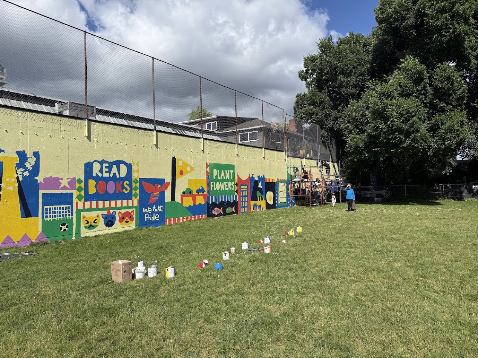 Volunteers and paint cans in the field beside the 'Read Books' and 'Plant Flowers' panels